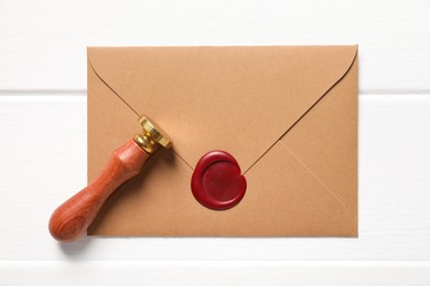 Photo of Envelope with wax seal and stamp on white wooden table, top view