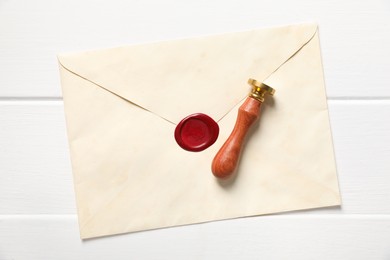Photo of Envelope with wax seal and stamp on white wooden table, top view