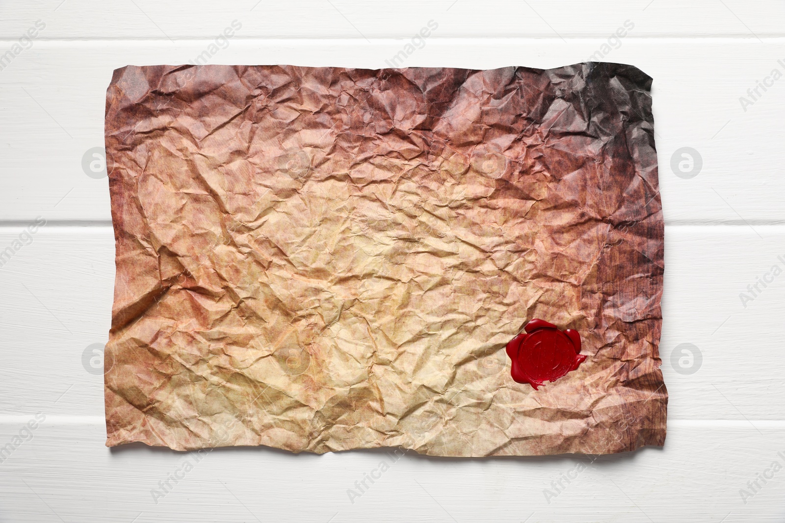 Crumpled paper with wax seal on white wooden table, top view Photo of Crumpled paper with wax seal on white wooden table, top view