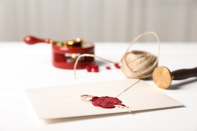Photo of Envelope with wax seal, twine and stamp on white table, closeup