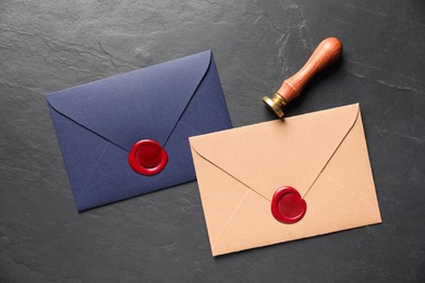 Photo of Envelopes with wax seals and stamp on black table, flat lay