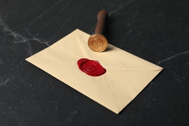Photo of Envelope with wax seal and stamp on black table, closeup