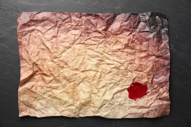 Photo of Crumpled paper with wax seal on black table, top view
