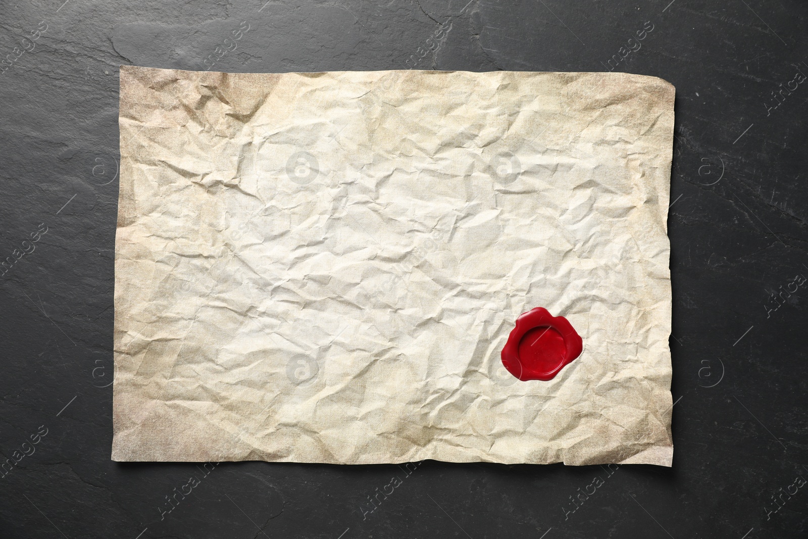 Crumpled paper with wax seal on black table, top view Photo of Crumpled paper with wax seal on black table, top view
