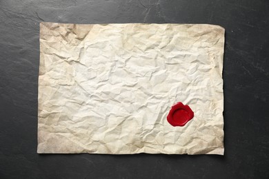 Photo of Crumpled paper with wax seal on black table, top view