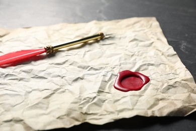 Photo of Crumpled paper with wax seal and fountain pen on black table, closeup