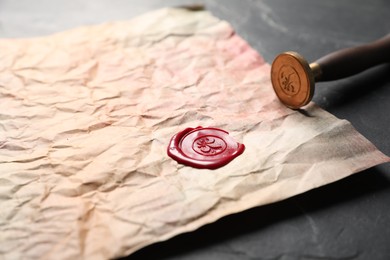 Photo of Crumpled paper with wax seal and stamp on black table, closeup