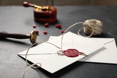 Photo of Envelopes with wax seal, twine and stamp on black table, closeup