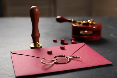 Photo of Envelope with wax seal, twine and stamp on black table, closeup
