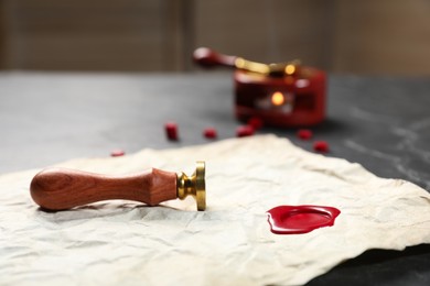 Photo of Crumpled paper with wax seal and stamp on black table, closeup