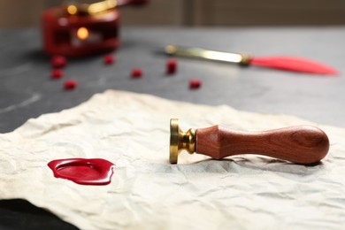 Photo of Crumpled paper with wax seal and stamp on black table, closeup