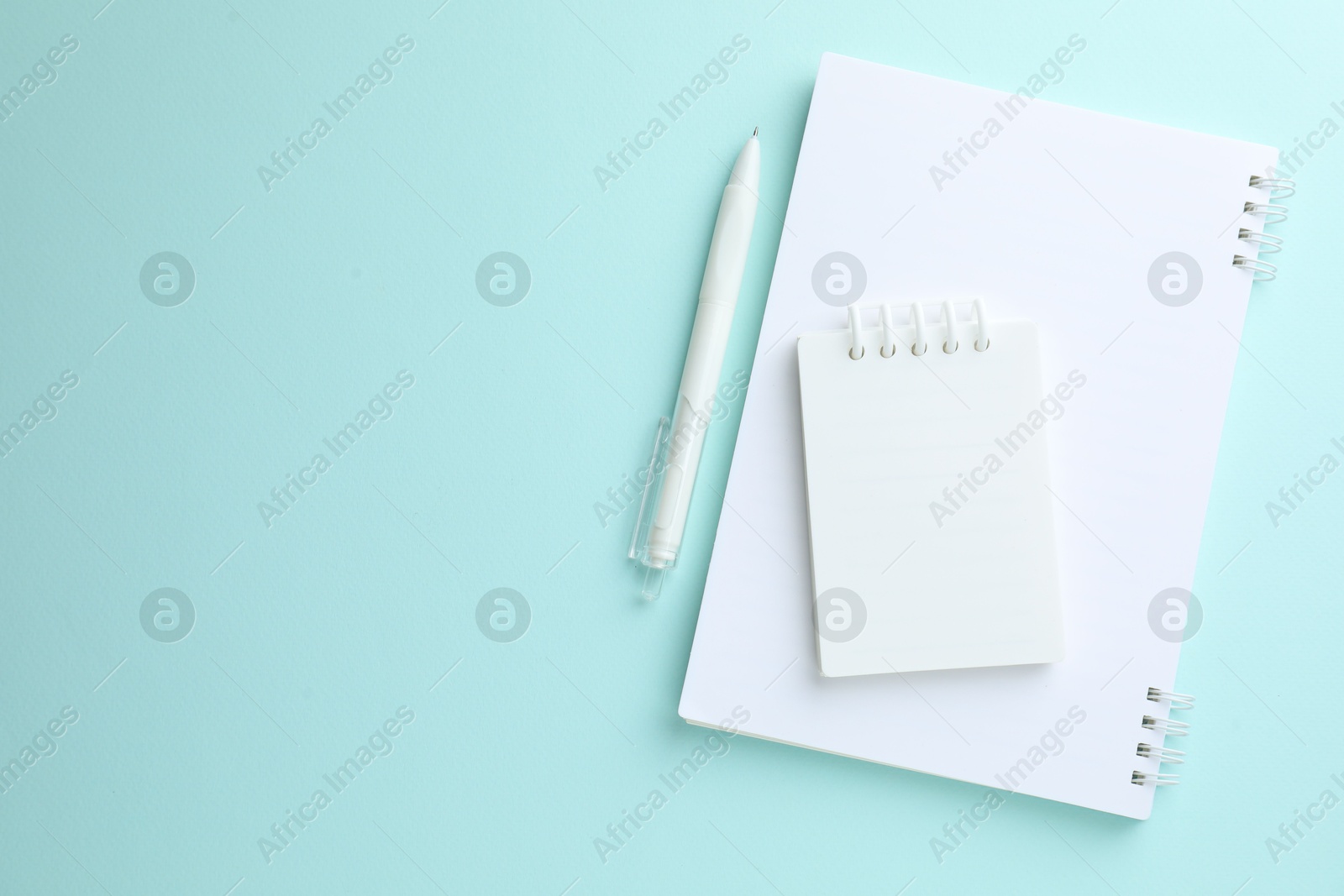 Photo of White notebooks and pen on light blue background, flat lay. Space for text