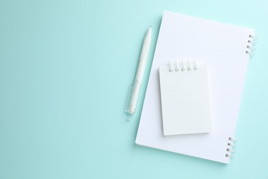 Photo of White notebooks and pen on light blue background, flat lay. Space for text