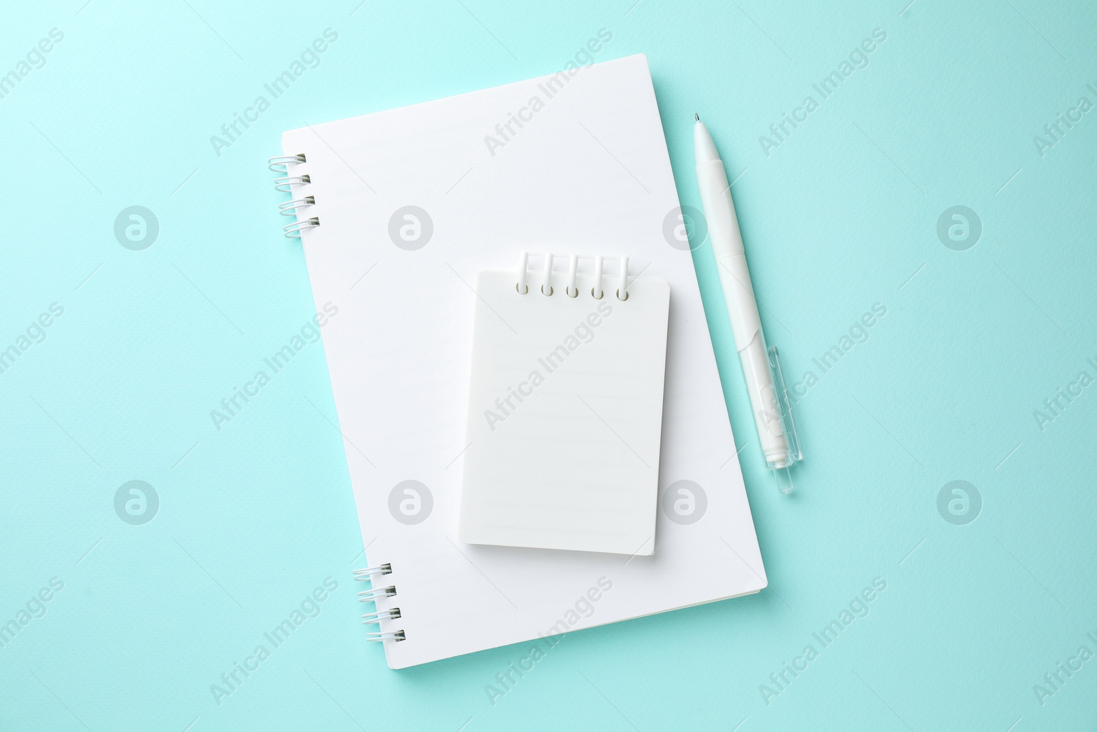 Photo of White notebooks and pen on light blue background, flat lay