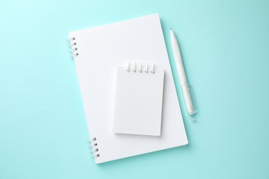 Photo of White notebooks and pen on light blue background, flat lay