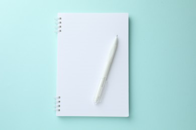 Photo of White notebook and pen on light blue background, top view