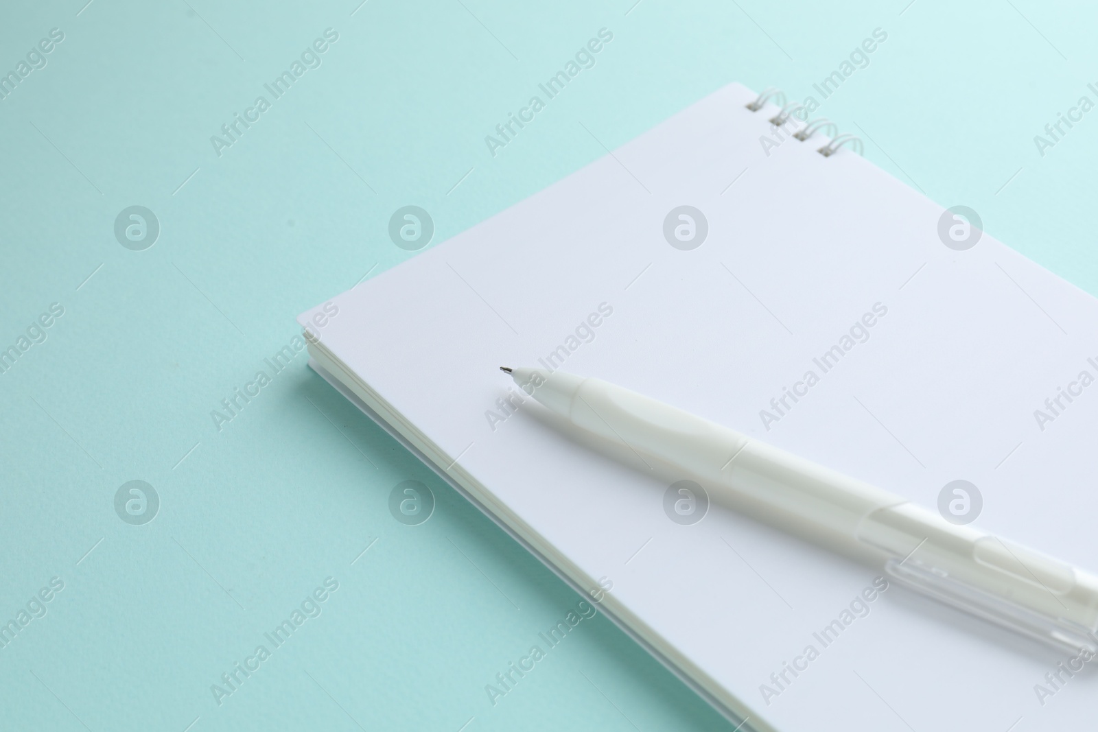 White notebook and pen on light blue background, closeup. Space for text Photo of White notebook and pen on light blue background, closeup. Space for text