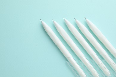 Photo of White pens on light blue background, flat lay. Space for text