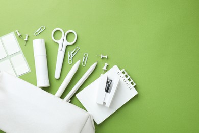Photo of White pencil case and different stationery on green background, flat lay. Space for text