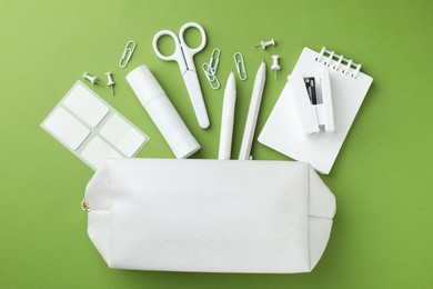 Photo of White pencil case and different stationery on green background, flat lay