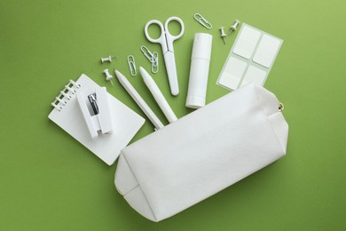 Photo of White pencil case and different stationery on green background, flat lay