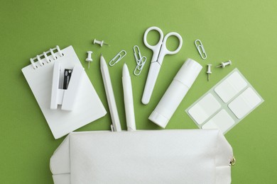 Photo of White pencil case and different stationery on green background, flat lay