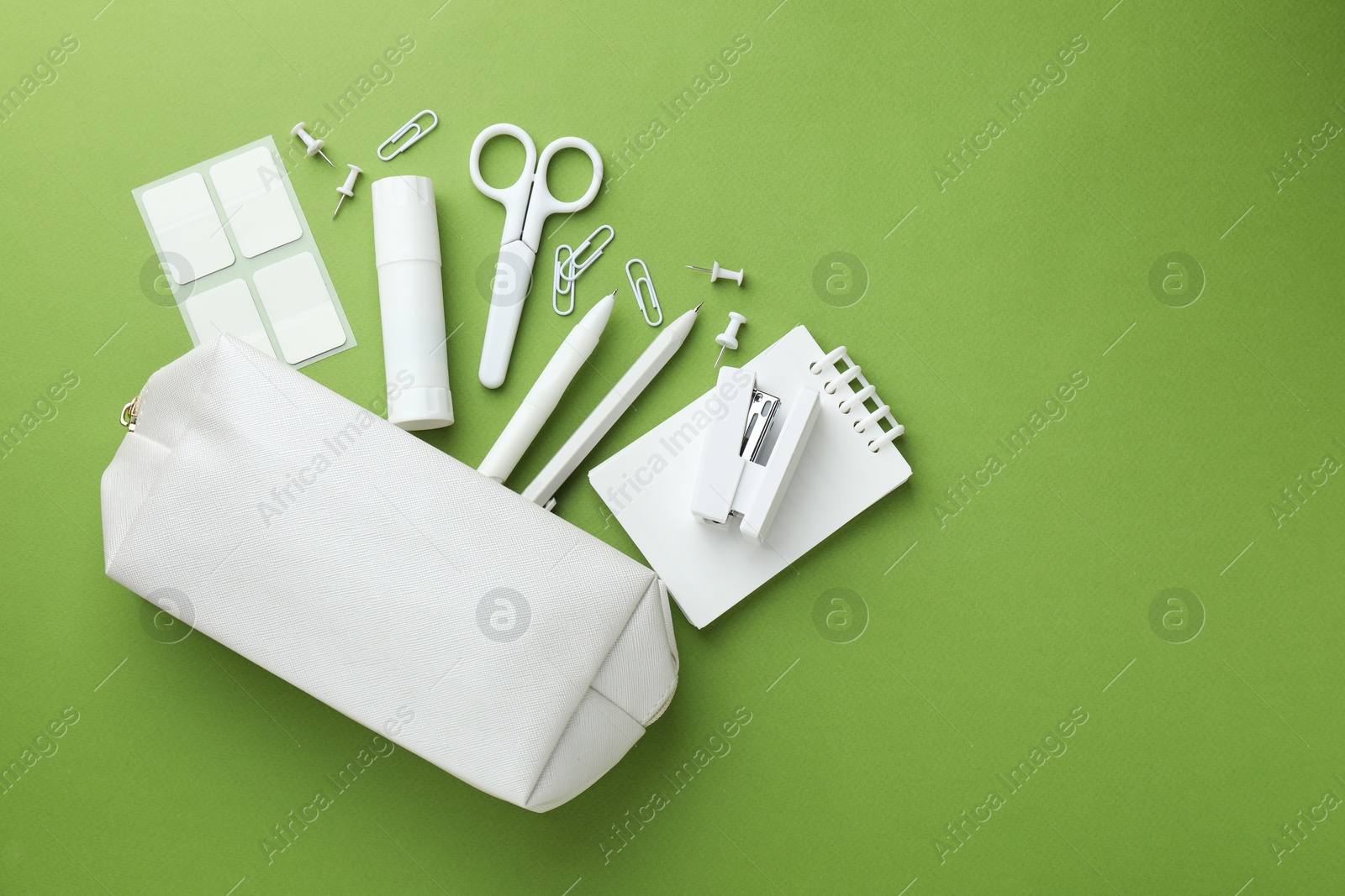 White pencil case and different stationery on green background, flat lay. Space for text Photo of White pencil case and different stationery on green background, flat lay. Space for text