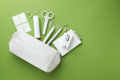 Photo of White pencil case and different stationery on green background, flat lay. Space for text