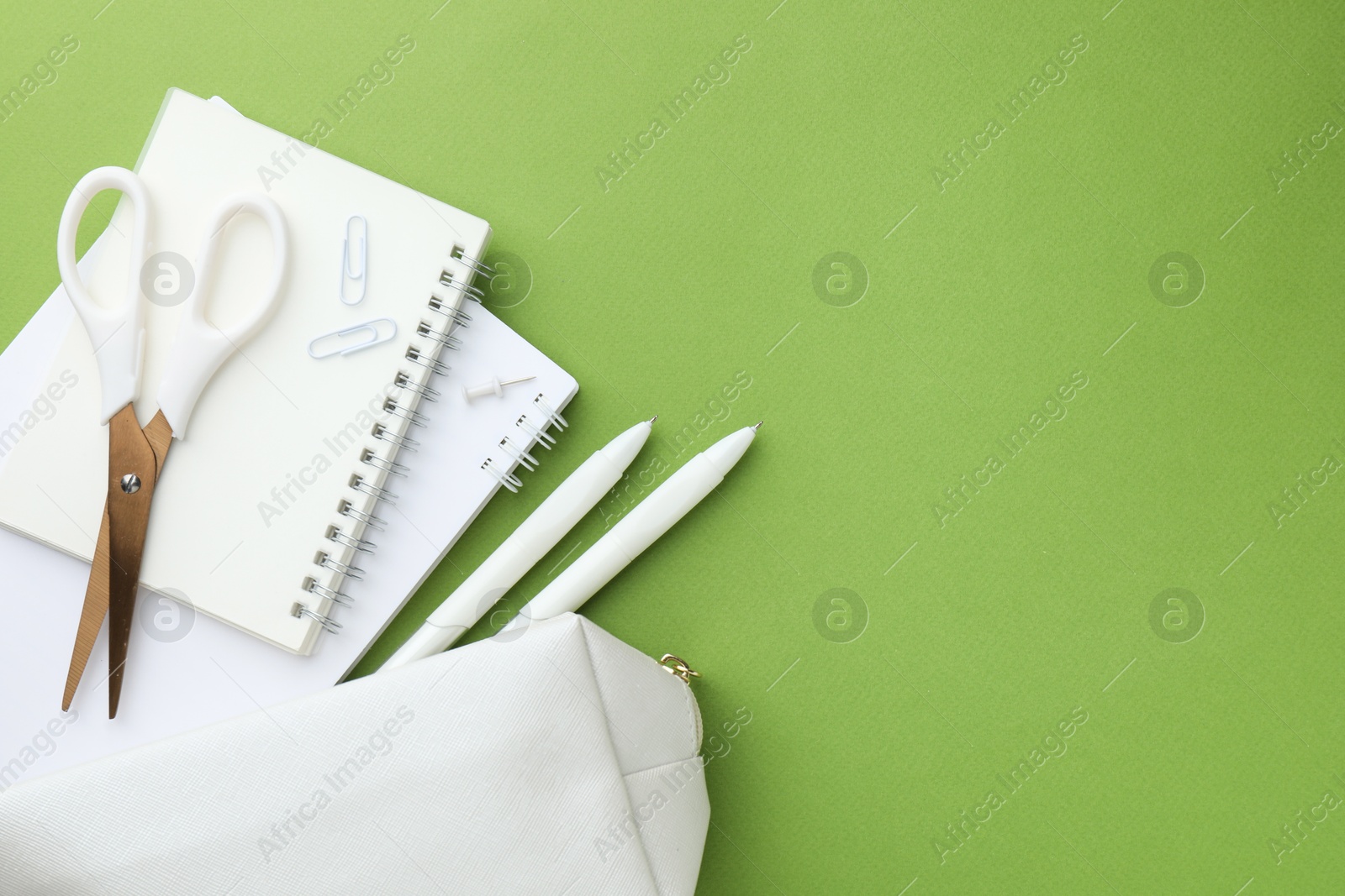 Photo of White pencil case and different stationery on green background, flat lay. Space for text