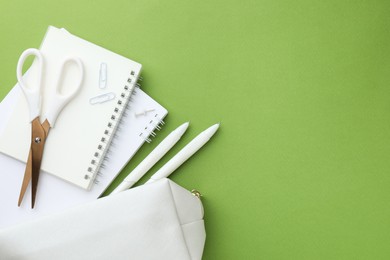 Photo of White pencil case and different stationery on green background, flat lay. Space for text