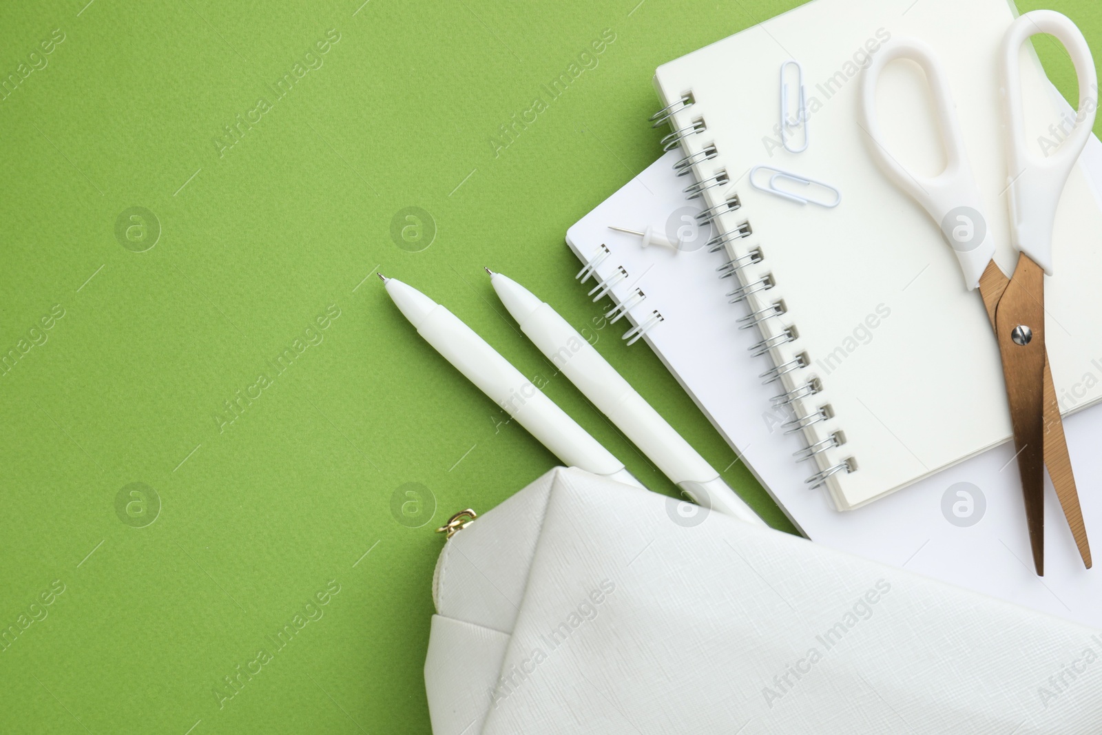 Photo of White pencil case and different stationery on green background, flat lay. Space for text