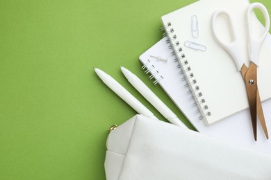 Photo of White pencil case and different stationery on green background, flat lay. Space for text