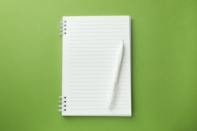 Photo of White notebook and pen on green background, top view