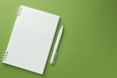 Photo of White notebook and pen on green background, flat lay. Space for text