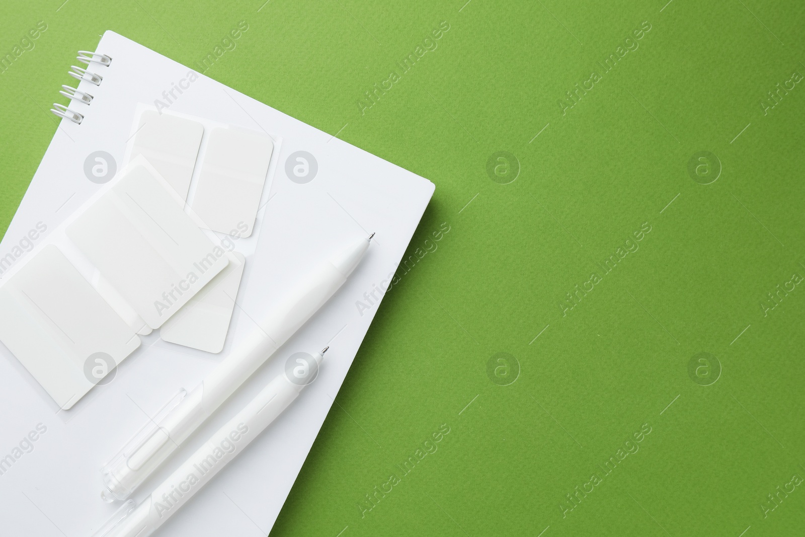 White notebook and other stationery on green background, top view. Space for text Photo of White notebook and other stationery on green background, top view. Space for text