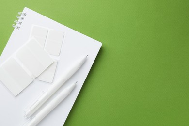 Photo of White notebook and other stationery on green background, top view. Space for text
