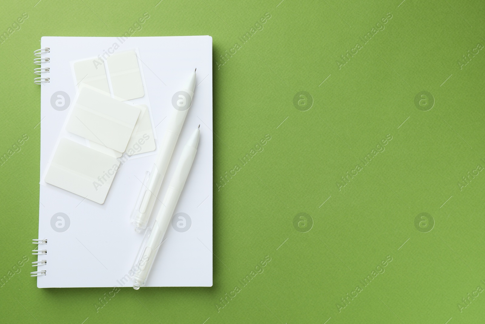 Photo of White notebook and other stationery on green background, top view. Space for text