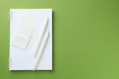 Photo of White notebook and other stationery on green background, top view. Space for text