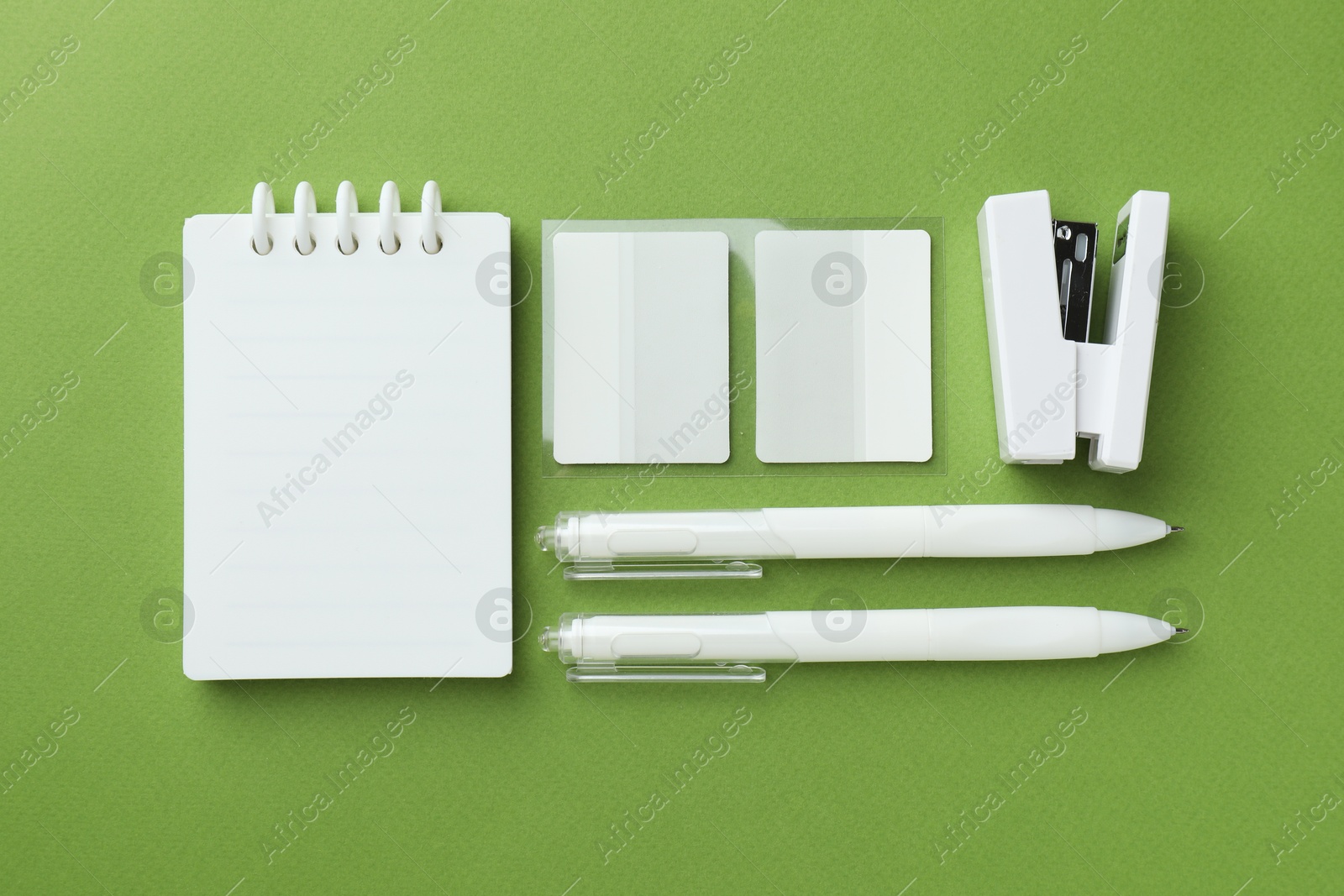 Photo of White notebook and other stationery on green background, flat lay