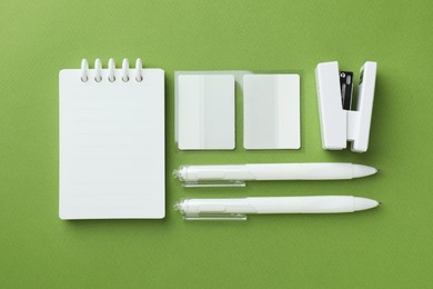 Photo of White notebook and other stationery on green background, flat lay