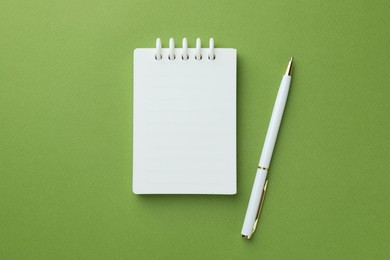 Photo of White notebook and pen on green background, flat lay