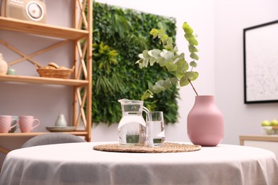 Photo of Stylish table with jug of water, glass and floral decor in dining room. Interior design