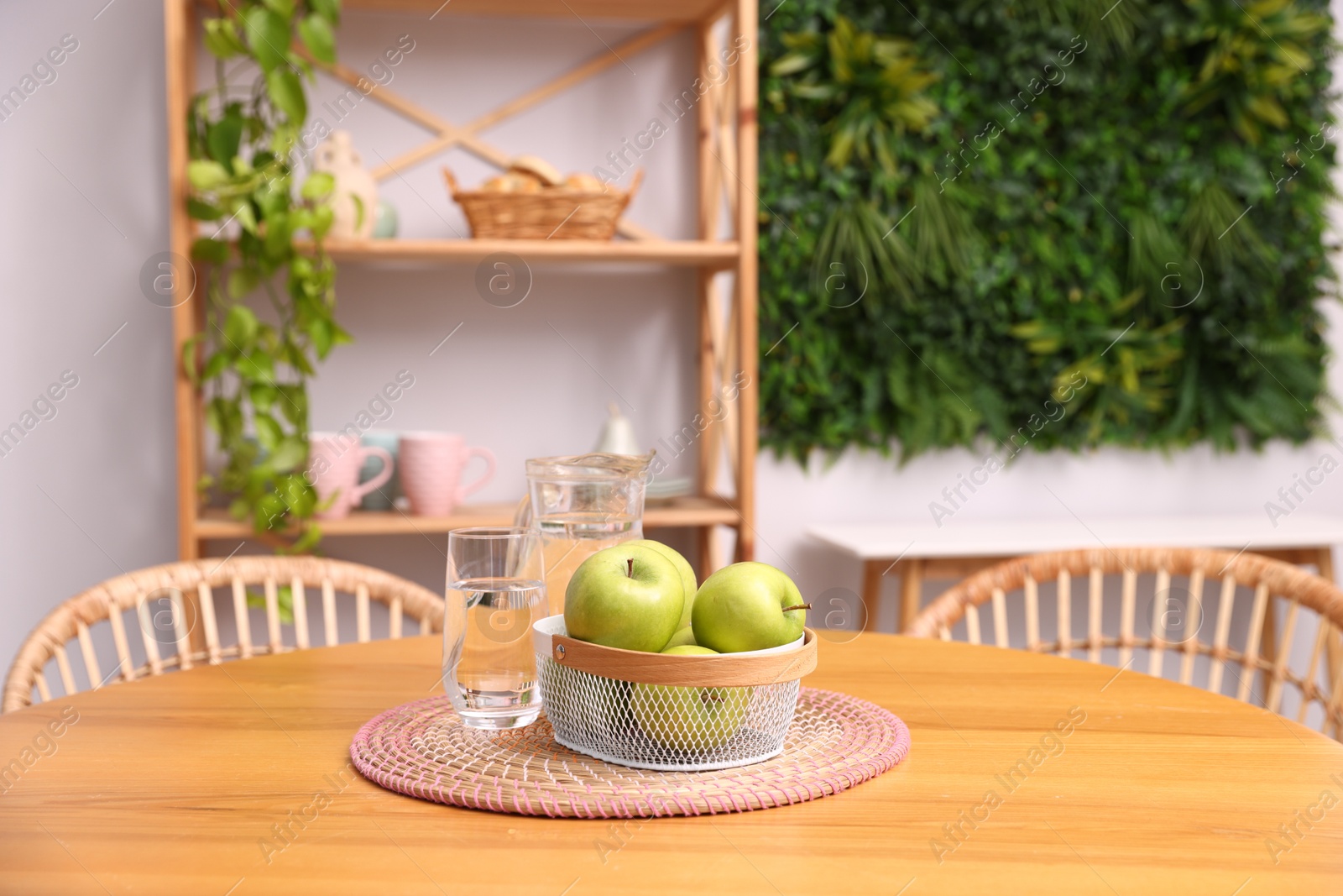 Photo of Wooden table with apples, jug of water, glass and chairs in stylish dining room. Interior design