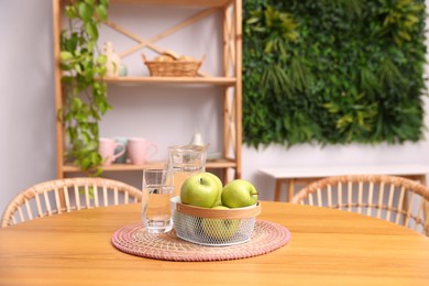 Photo of Wooden table with apples, jug of water, glass and chairs in stylish dining room. Interior design