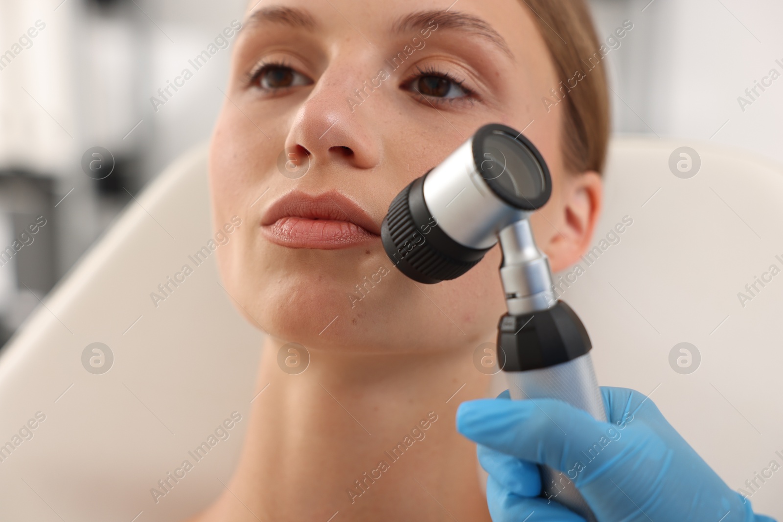 Doctor examining young woman's mole with dermatoscope in hospital, closeup Photo of Doctor examining young woman's mole with dermatoscope in hospital, closeup