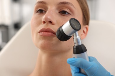Photo of Doctor examining young woman's mole with dermatoscope in hospital, closeup