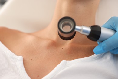 Photo of Doctor examining young woman's mole with dermatoscope in hospital, closeup
