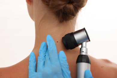 Photo of Doctor examining young woman's mole with dermatoscope on white background, closeup