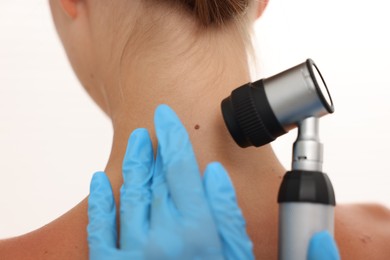 Photo of Doctor examining young woman's mole with dermatoscope on white background, closeup