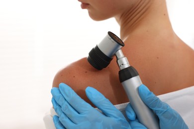 Photo of Doctor examining young woman's mole with dermatoscope on white background, closeup